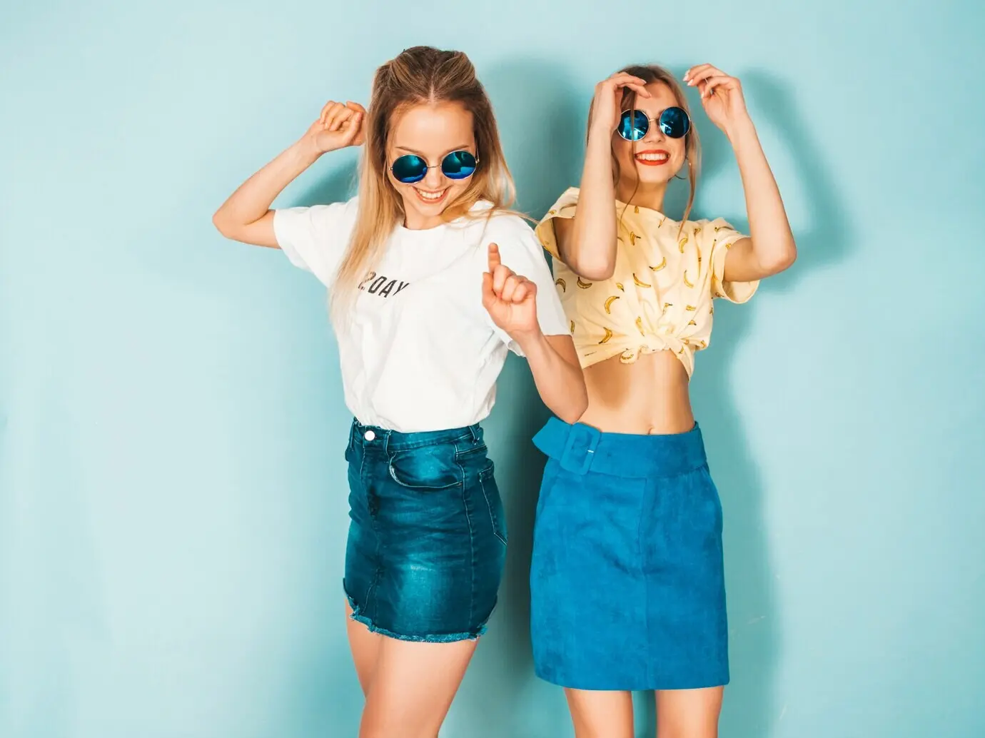 Zwei junge, schöne, lächelnde, blonde Hipster-Mädchen in trendigen Sommer-Jeansrock-Outfits.